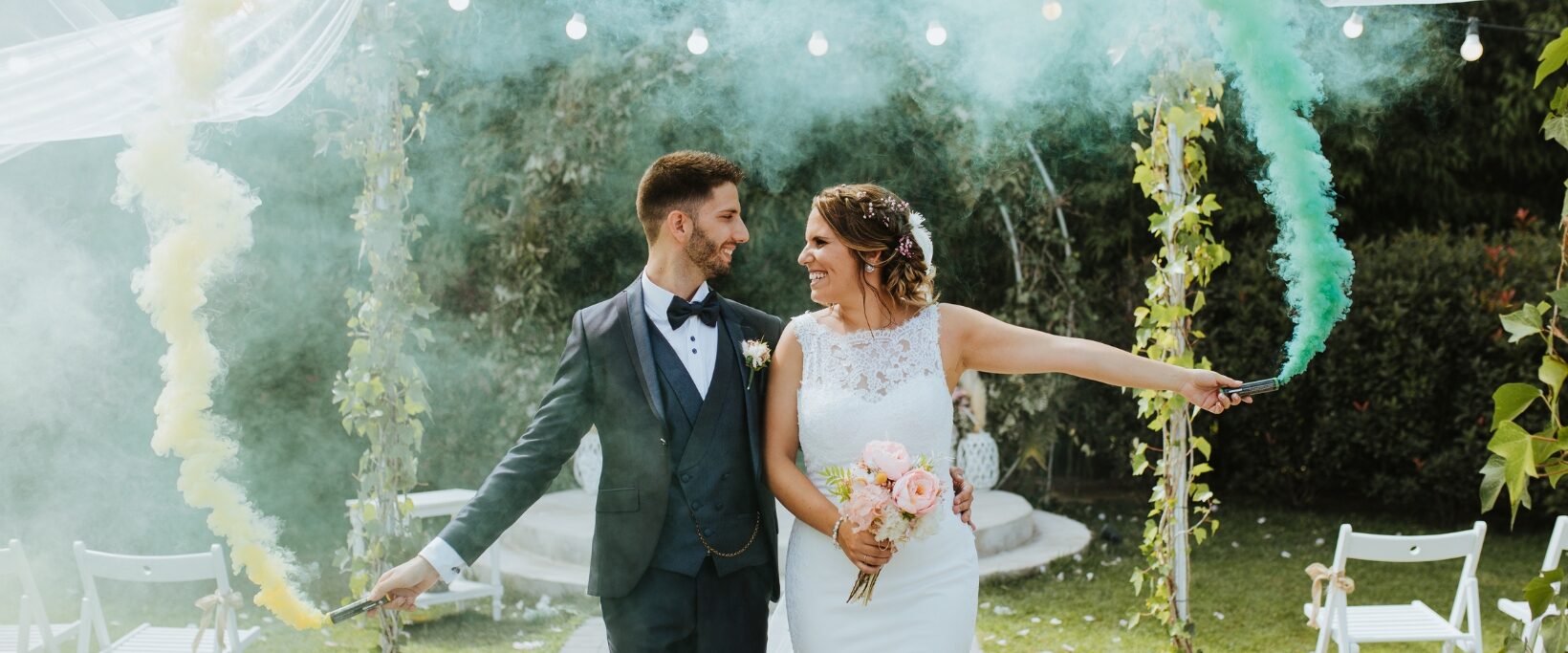 Dos novias en ceremonia al aire libre con arco floral – Love Agency Barcelona Dos novias tomadas de la mano frente a arco floral en ceremonia de boda al aire libre, Love Agency wedding planner Barcelona